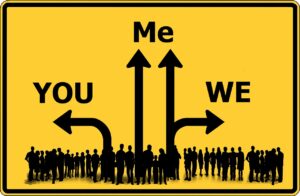 A graphical image of a road sign displaying single arrows pointing right and left with words 'you' and 'we' respectively and double arrows pointing upwards with the word 'me' above and a silhouette of a large group of people at the base of the arrows