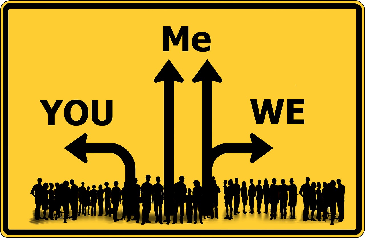 A graphical image of a road sign displaying single arrows pointing right and left with words 'you' and 'we' respectively and double arrows pointing upwards with the word 'me' above and a silhouette of a large group of people at the base of the arrows