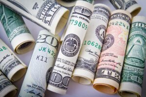 A close up photo of many rolls of U. S. money in different denominations laying together on a plain white flat surface