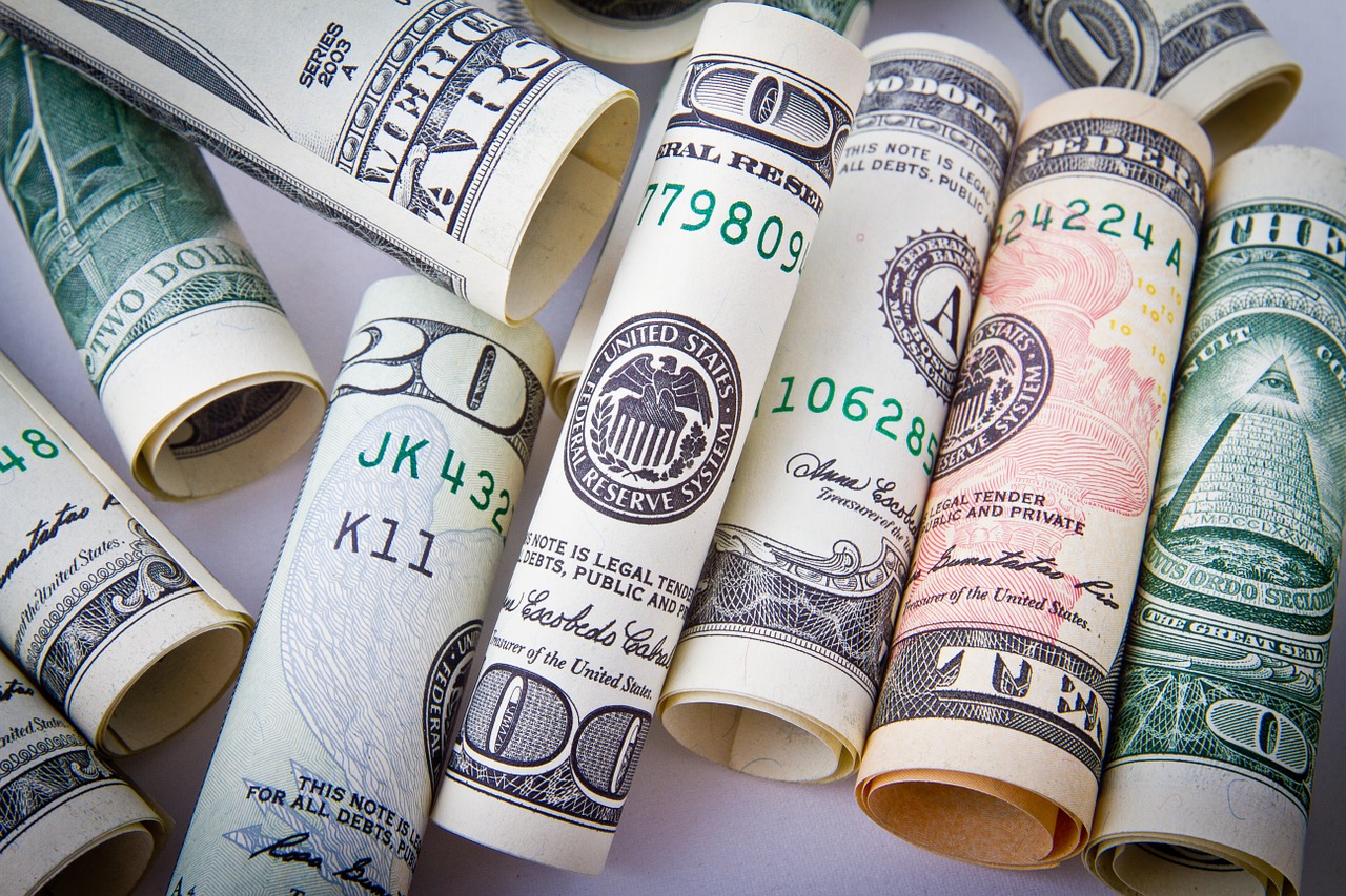 A close up photo of many rolls of U. S. money in different denominations laying together on a plain white flat surface