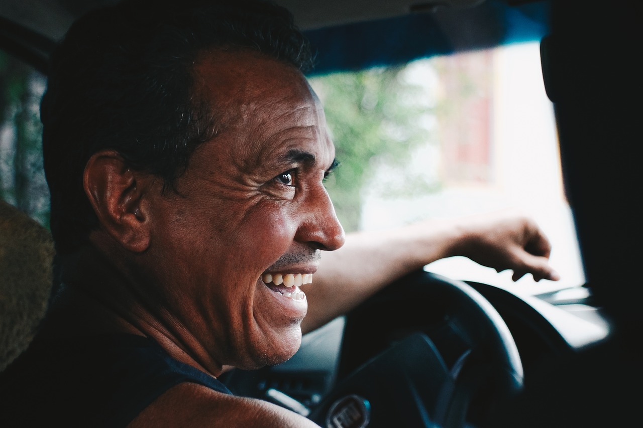 A photo of the side view of a headshot of man seated in the driver's seat of a car while laughing