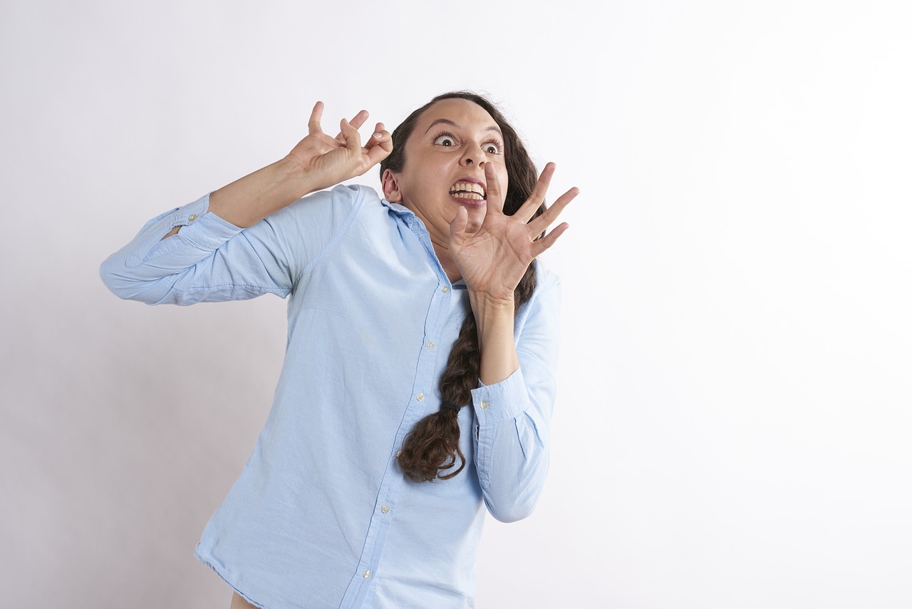 A photo of a young woman in a light blue long-sleeved buttoned shirt recoiling in fear against an unseen object