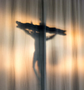 A photo of an illuminated crucifix behind a white pleated curtain