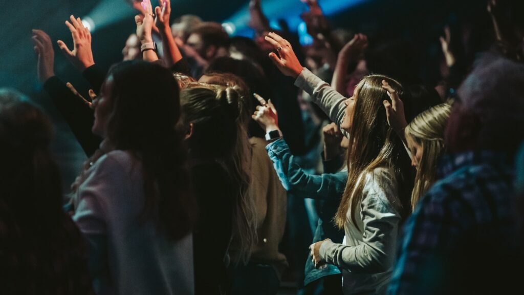 A photo of the backside of a group of people with hands raised in worship in a large room