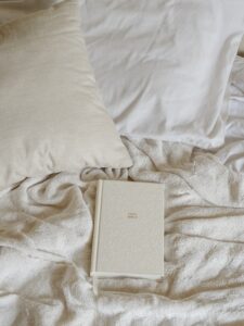 A photo of an off-white Bible laying in the midst of a bed covered with white and off-white sheets and pillows