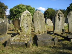 A cluster of old graves a gravestones in a cemetery with trees in the background and a blue sky
