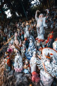 A photo of a very large number of assorted idols of a steep rocky hillside with trees in the background