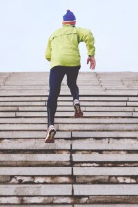 Backside of a person running up stone stairs in dark blue pants, pale yellow jacket, and blue/red knit hat