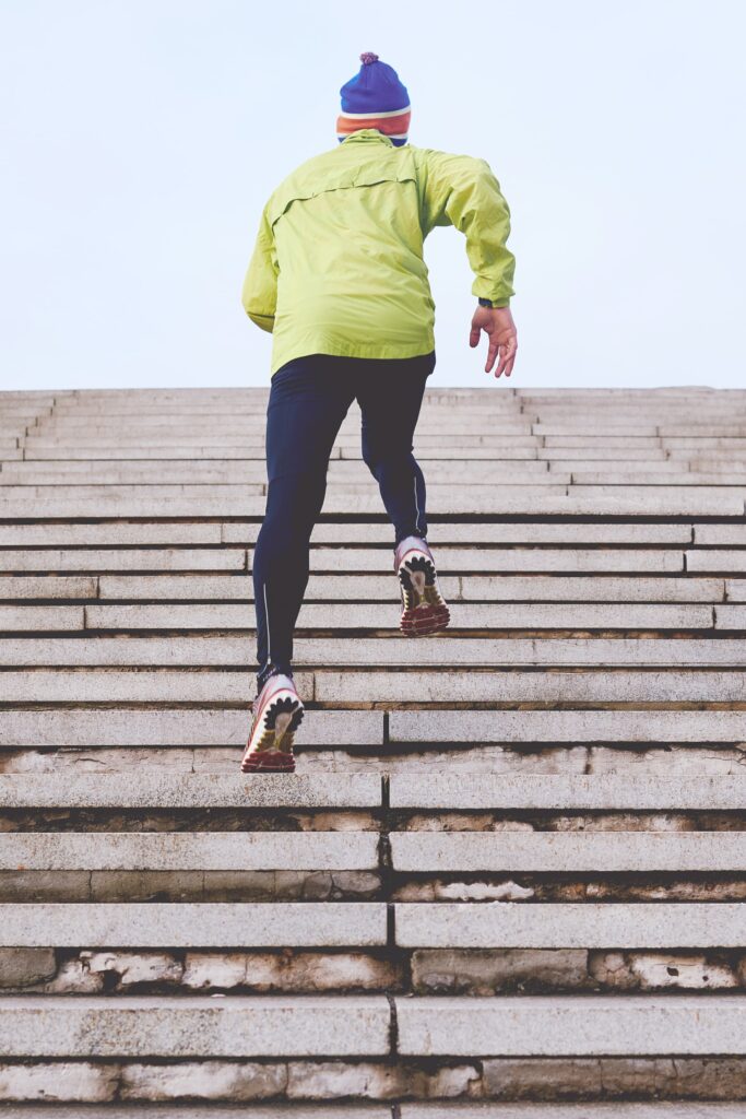 Backside of a person running up stone stairs in dark blue pants, pale yellow jacket, and blue/red knit hat