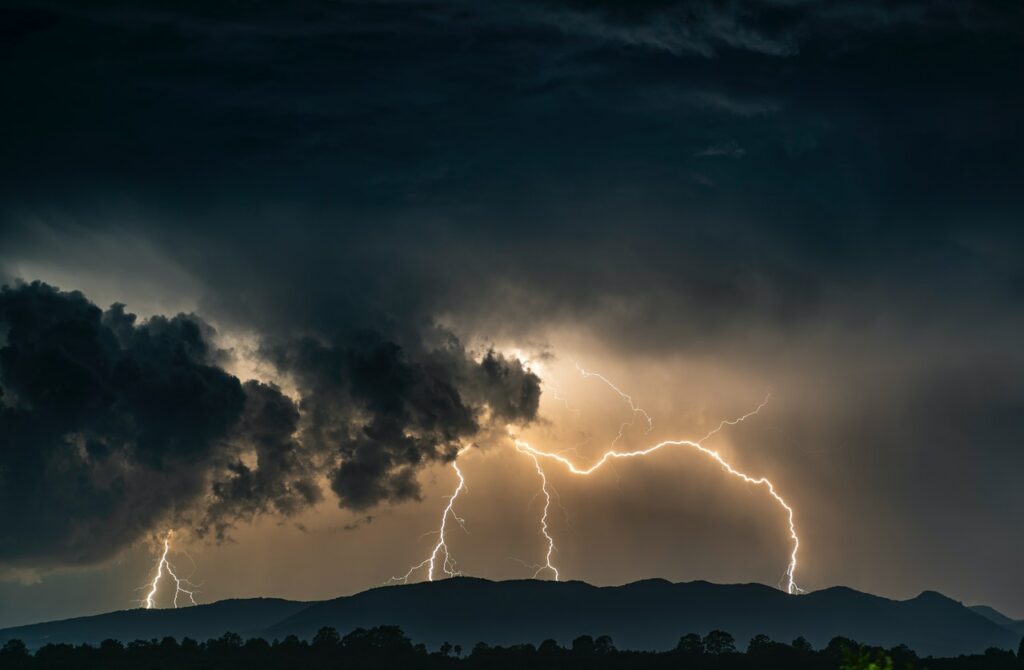 An evening thunderstorm with dark clouds and several bolts of lightning striking a mountain range in the background