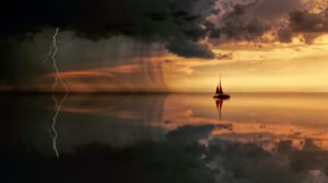 A sailboat in the distance on a large calm body of water with a thunderstorm on the left and a sunset on the right