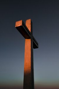 A photo of a large wooden cross illuminated by a setting golden sun against a dark blue sky