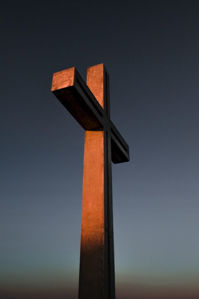 A photo of a large wooden cross illuminated by a setting golden sun against a dark blue sky