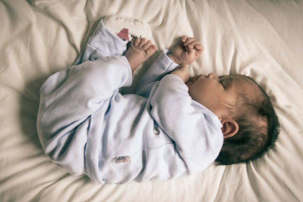 A photo of a sleeping baby laying on its side in a very light blue sleeper on a white sheet