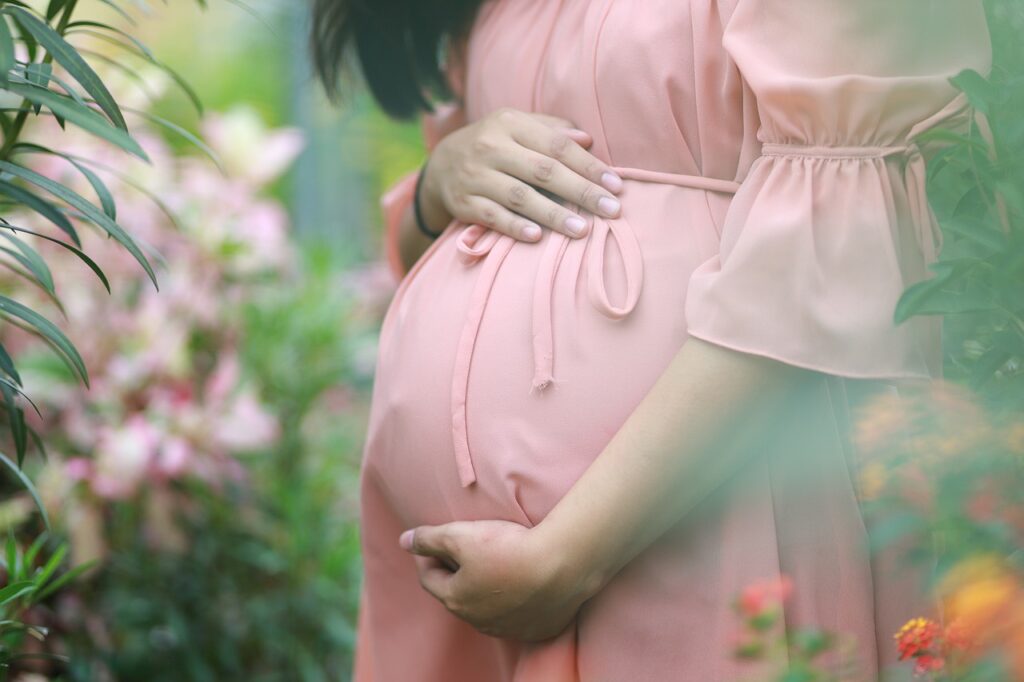 A cropped photo of the lower section of a woman with black hair and a pink dress holding her pregnant abdomen symbolic of how God spiritually states in the heart of the child that, I love you