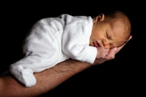 A photo of an infant wearing a sleeper while sleeping on a man's outstretched arm