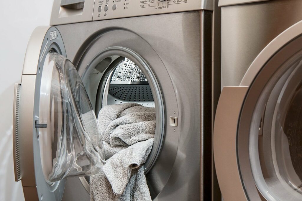 A photo of a front loading stainless steel washing machine with the door open and a white towel partially draped outside, an example of the fact the God's grace is not like a washing machine