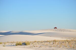 A desert scene with a small tent on a large dune in the background against a cloudless blue sky
