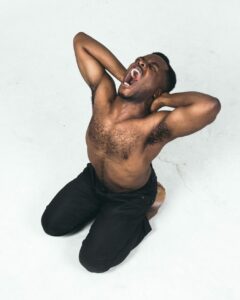 A solitary African or African-American man on his knees screaming and looking up with closed eyes and hands against the backside of his neck.
