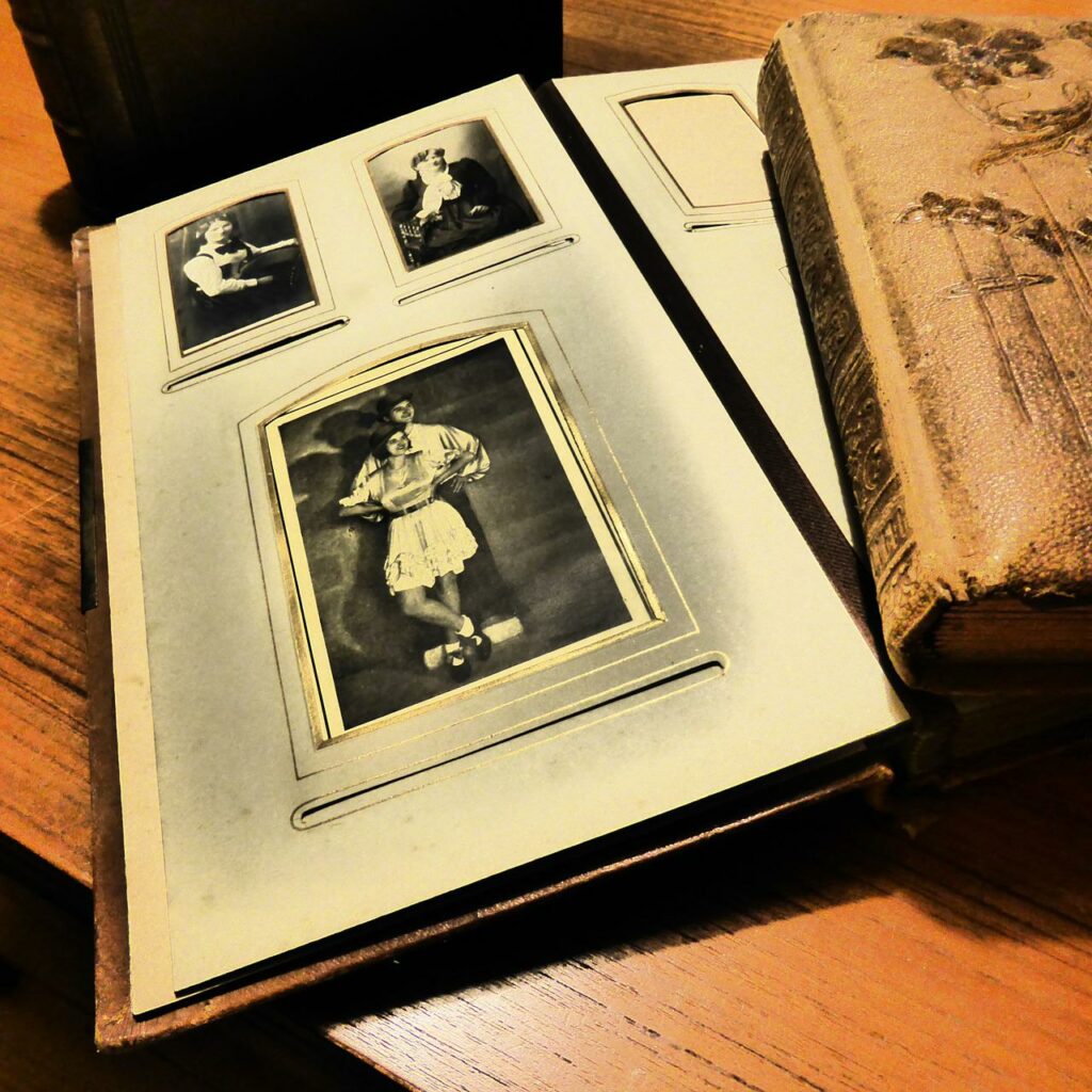 A open page of an old photo album laying flat with another book on an old wood desk with a bright light overhead