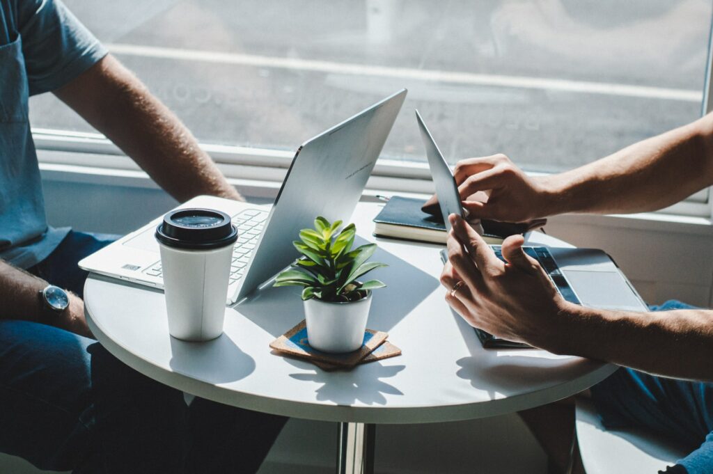 Two men working on laptop computers in front of a sunny window