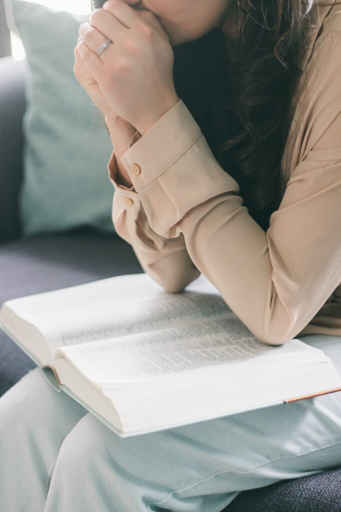 A woman seated, leaning over an open Bible with arms folded in prayer reminding us that when we seek God we will find help from trouble