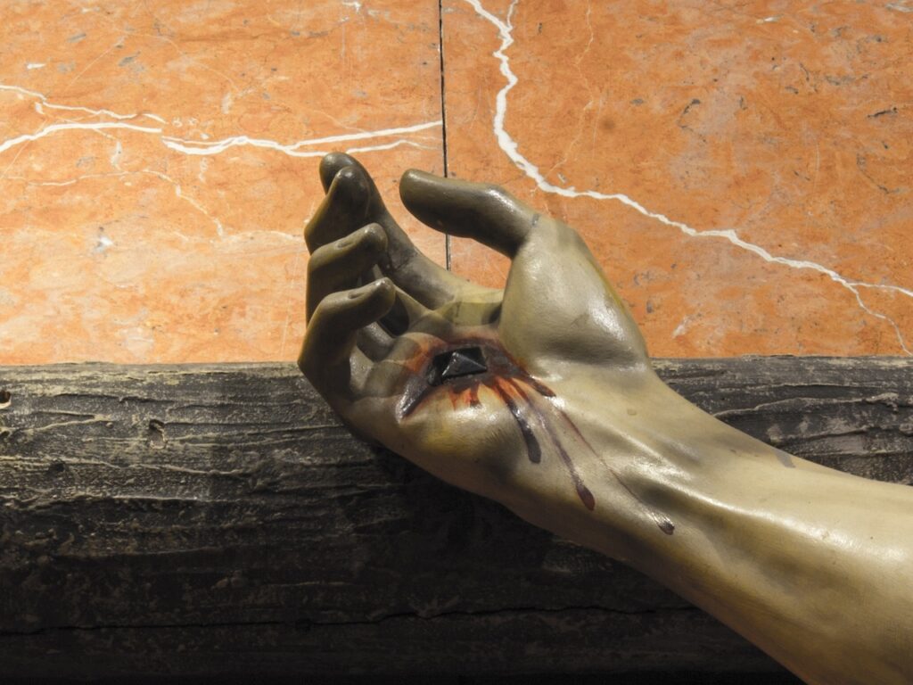 A photo of a part of a statue showing the hand of Jesus on the cross depicting the shed blood of Christ