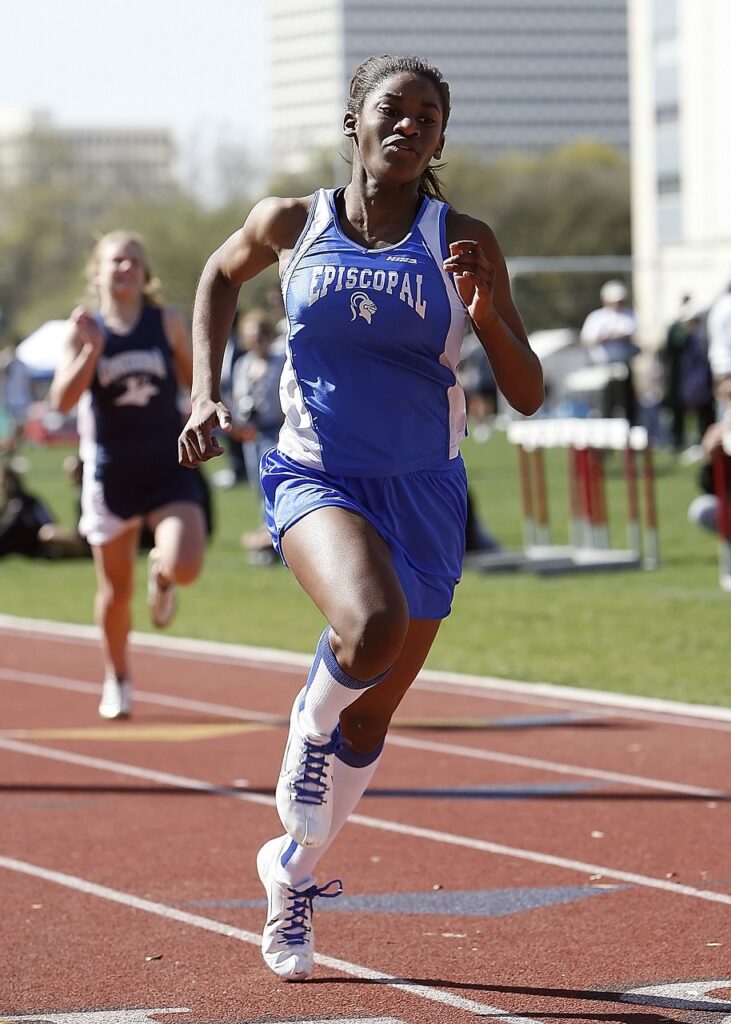 An African-American woman running in a race and taking the lead by not being complacent.
