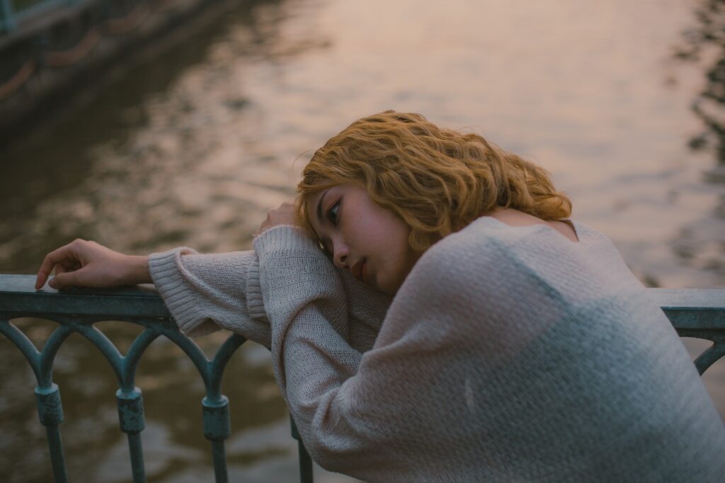 A young woman leaning hear head against a railing with a depressed appearance and the feeling the she has been forgotten by God