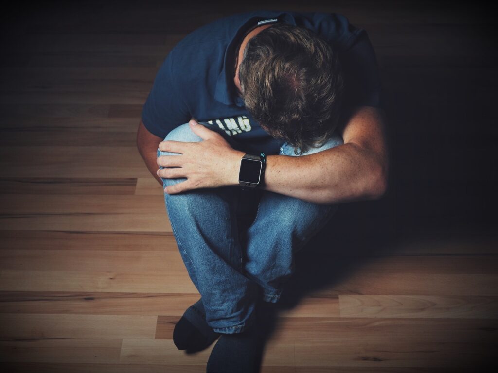 A photo of a man seated with a leaning down against folded legs in a depressed expression not showing the joy of the Lord.