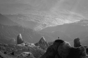 A person under a shadow on a mountain top among many othe mountains and hills.