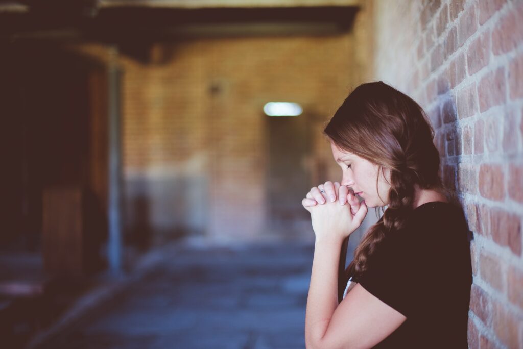 Woman leaning against a brick wall in prayer and gaining victory over her spiritual struggle.