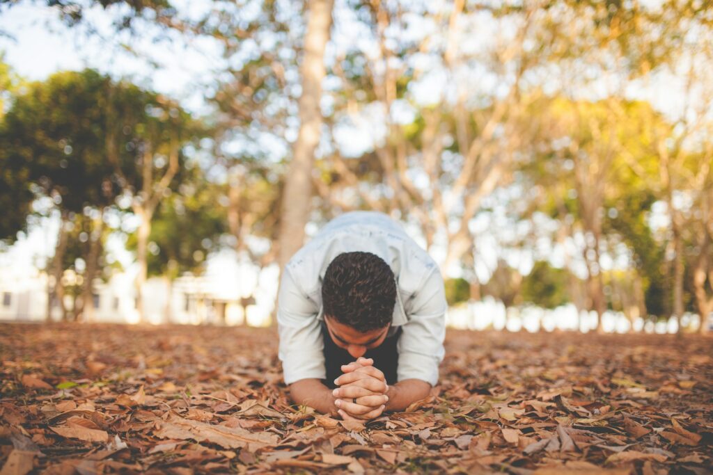 A man bowing on his knees seeking the peace of God while in a leaf strewn area