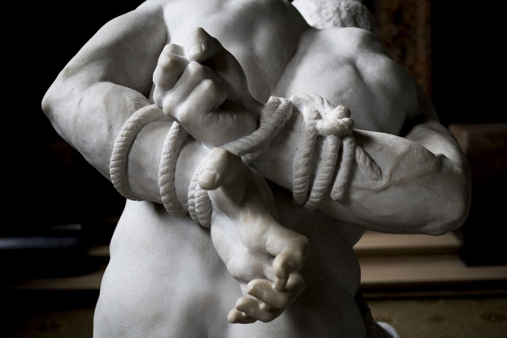 the backside of sculpture of a man whose arms are tied up with rope, symbolizing how our old self keeps us bound in sin