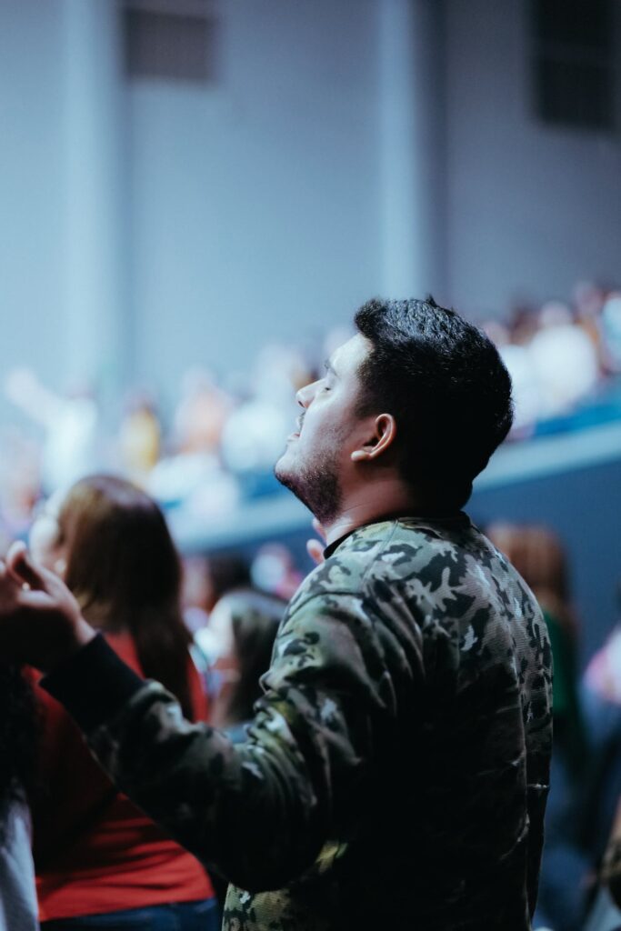 Man in auditorium with eye closed and hands raised in the air in worship and praise demonstrating that God is worthy of our praise