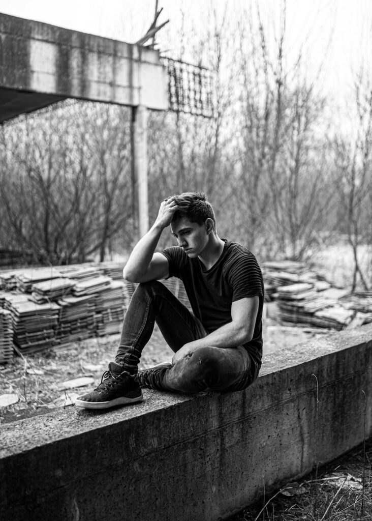 A man sitting on a concrete wall with his hand against his head with a depressed expression on his face typifying how a lack of faith in Jesus will leave one in despair.