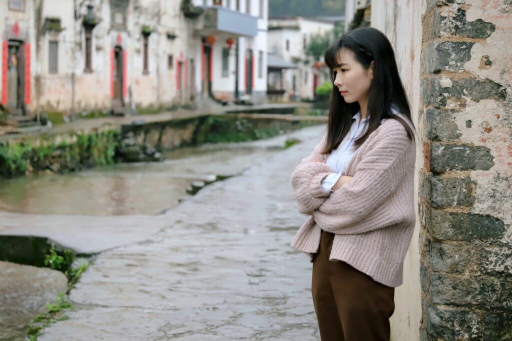 upset Asian woman leaning against a wall in a small village