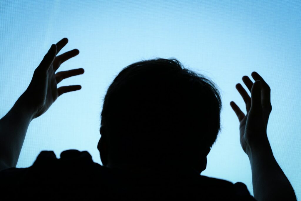 A silhouette of a man with hands upward worshipping God with a solid light blue background