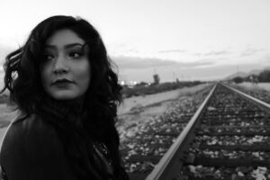 black and white photo of a woman standing next to a railroad track while looking forward at something to her right