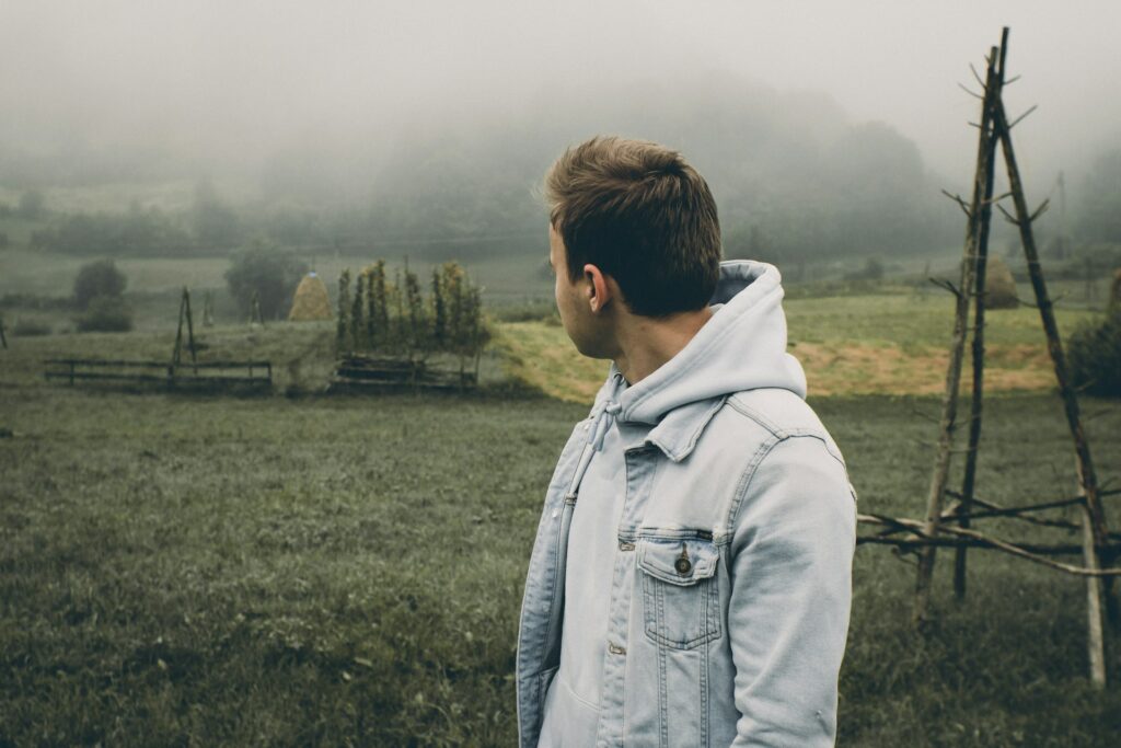 A young man casually dressed looking back over a green field with fog in the background