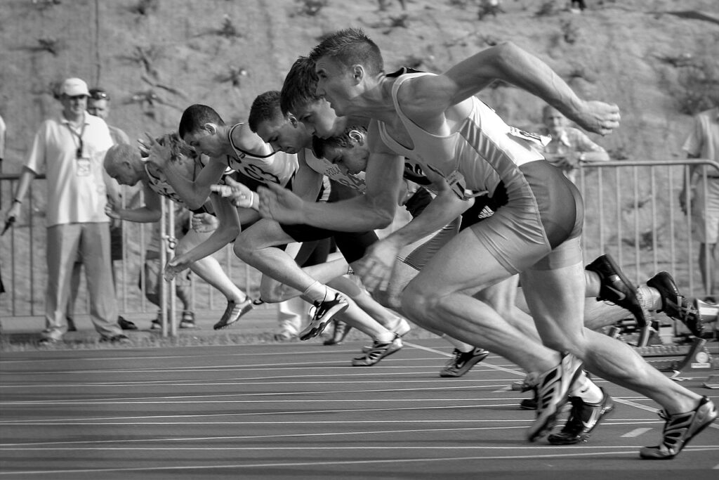 A black and white photo of a side view of a group of track runners just taking off form the starting line who know the results of when you forget your past and focus on the prize ahead