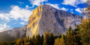 a large rock mountain with trees in the background with El Capitan in the background