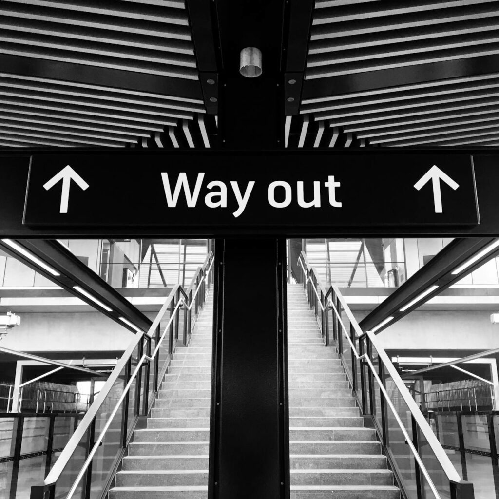 A sign over a tall staircase of a building with the words, Way Out, indicating a way to escape