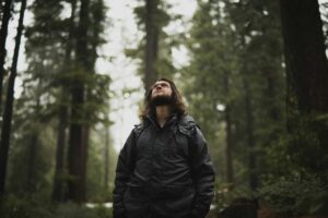 man-in-forest-looking-up-corey-agopian-eovZHPLjsb0-unsplash(https-::unsplash.com:photos:man-wearing-black-jacket-looking-up-surrounded-with-tall-trees-eovZHPLjsb0)