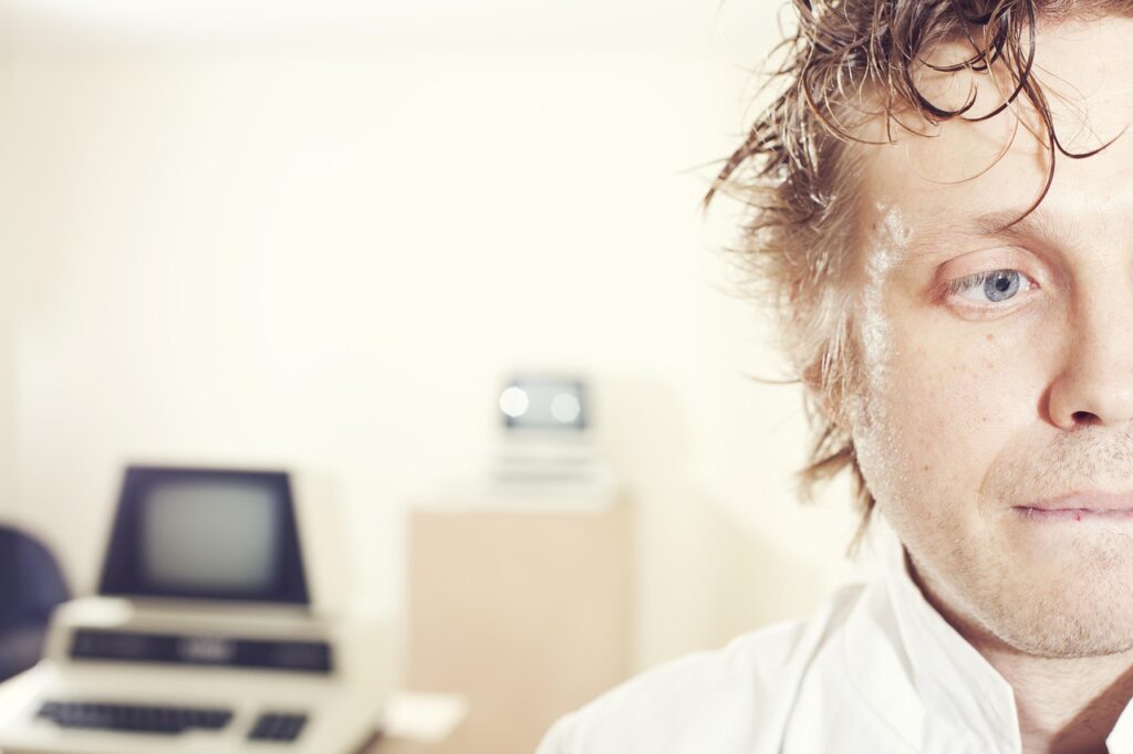 A man under stress and possibly failure with a computer terminal in the background