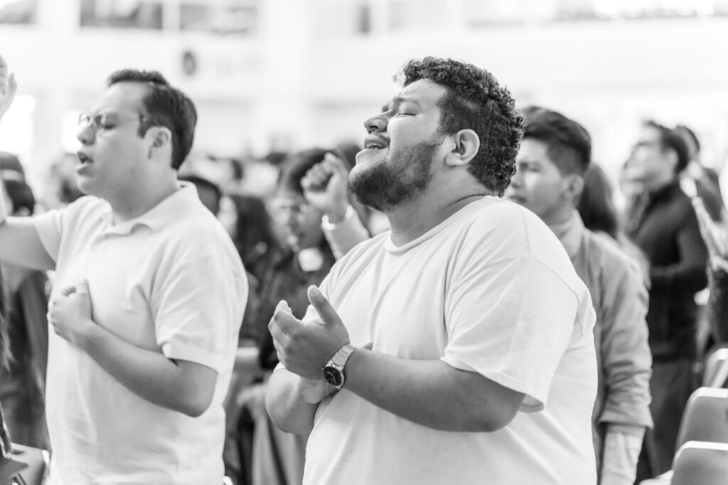 black & white photo of individuals singing with eyes closed in worship service